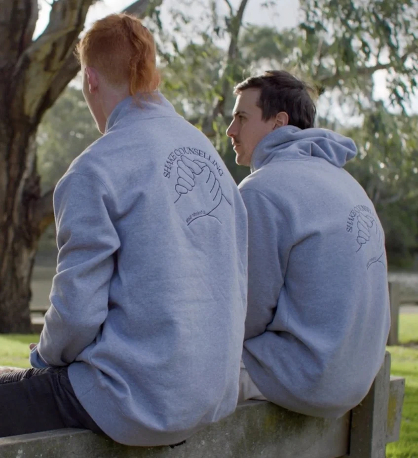 Rear view of two boys in gray Shake Counselling hoodies standing outside