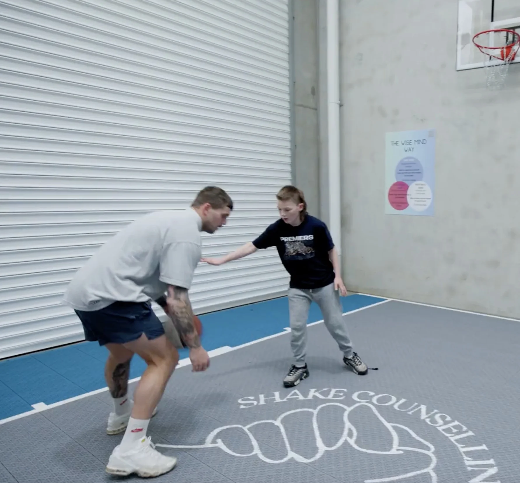 Two boys practicing basketball moves on court with Shake Counselling logo