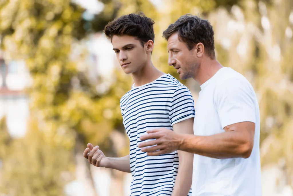 Serious father and troubled teenage son talking outdoors, representing potential need for teen counselling in Geelong