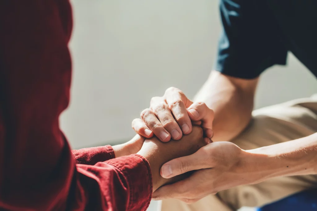 Two people holding hands in a supportive counselling session