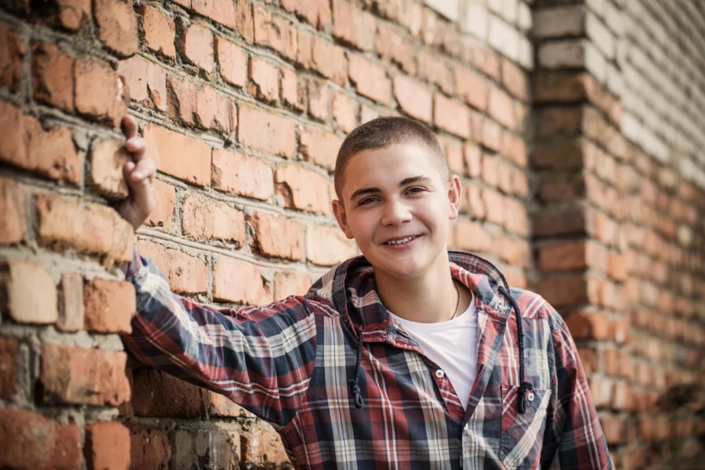 Smiling Geelong teen leaning against brick wall, representing youth supported by mentoring or counselling