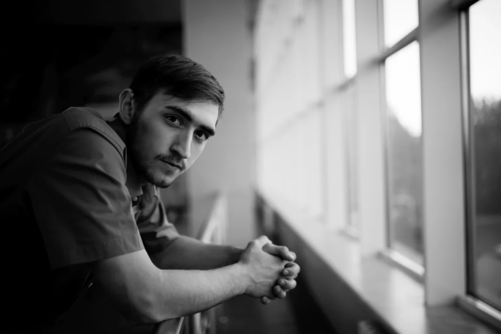 Thoughtful young man looking out a window, representing the self-reflection and growth fostered by peer mentors in Geelong