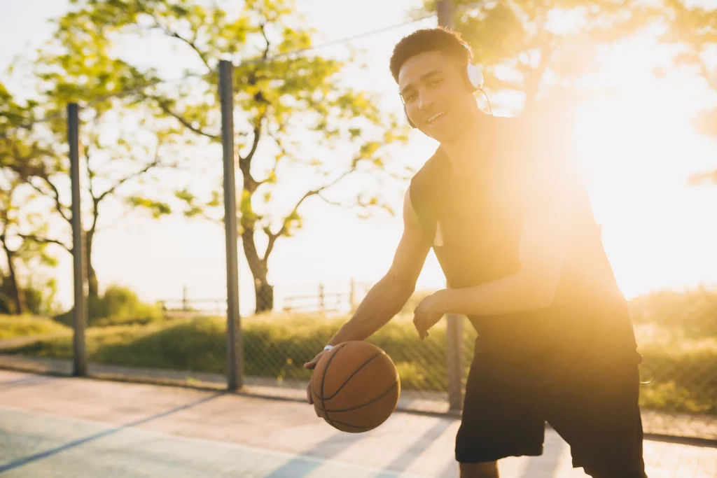 Teenage boy playing basketball outdoors at sunset, wearing headphones" Caption: "Our movement-based therapy combines physical activity with mental health support