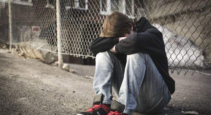 Teenager showing signs of depression and isolation, sitting alone against a fence in a withdrawn posture